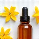 Flacon d'huile essentielle d'Ylang-Ylang à côté de ses fleurs jaunes tropicales.